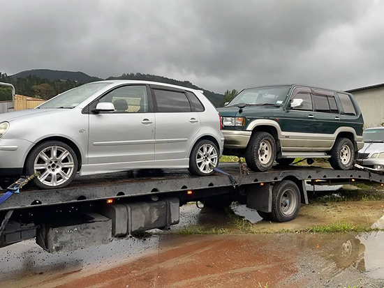 Tow truck transporting three scrap cars for removal in 0800 Car Salvage